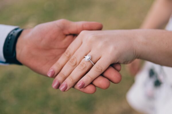 A man holds the hand of a woman wearing an engagement ring.